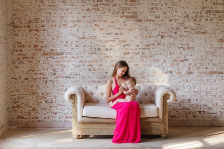 Mother breastfeeding baby sitting on sofa in loft design interior with brick wall on backgroundの写真素材
