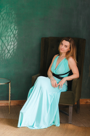 Portrait of beauty young woman on armchair in studio. Green empty wall on background, copyspaceの写真素材