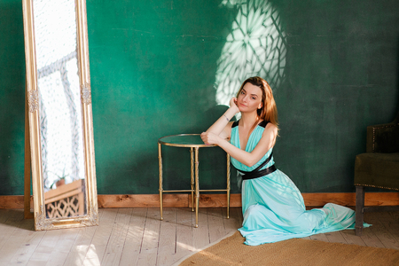 Beautiful blonde woman in the interior studio sits on floor. Green empty wall on background. Copyspaceの写真素材