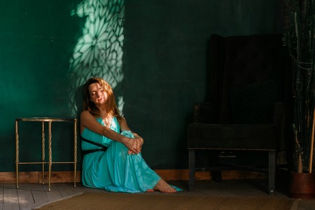 Sweet woman sits on floor barefoot against green wall. Relaxing in sunbeamsの写真素材