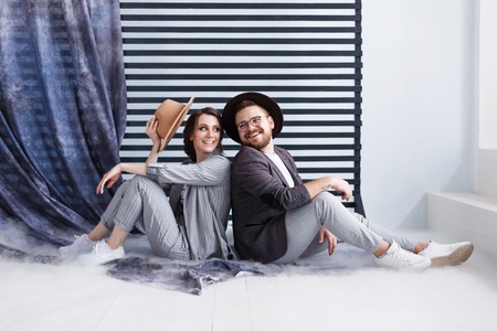 Cheerful young couple sitting with back to each other on floor, smiling happily. Black and white stripes on background.の写真素材
