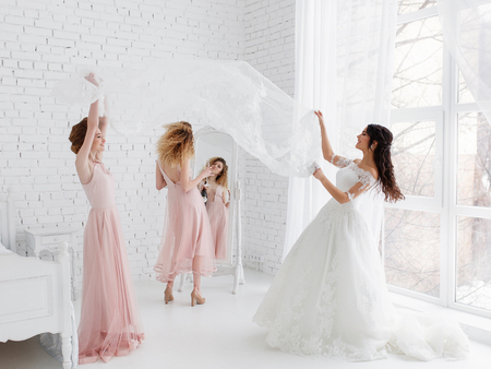 Cute girls celebrating a brides bachelorette party and playing with veil in bedroom.の写真素材
