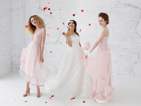 Bride and bridesmaids dancing in white studio with flying petals. Full-lenght portrait.