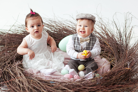 little girl and boy sitting in branch nest with easter eggsの写真素材