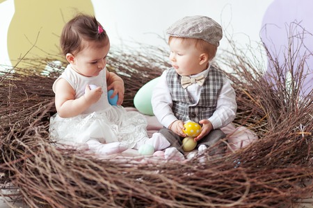 little girl and boy sitting in wooden natural nest with easter eggsの写真素材