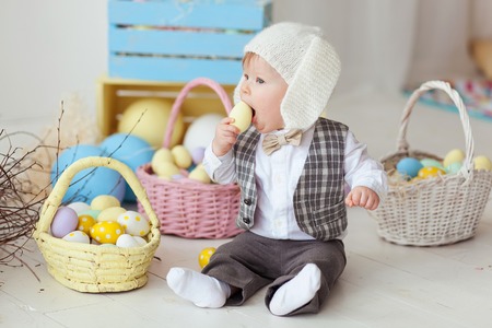 Funny happy baby boy in bunny hat, tie bow and suit playing with Easter eggs. Eating eggの写真素材