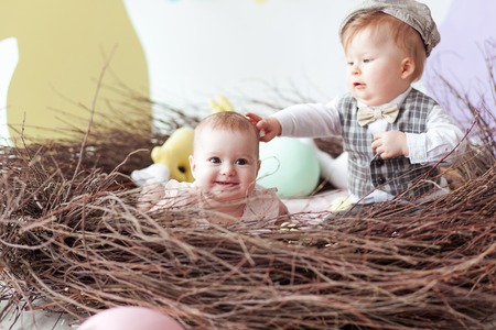 Little boy and girl sitting in natural nest with colorful Easter eggs. Home decoration - pastel color bunny bannerの写真素材