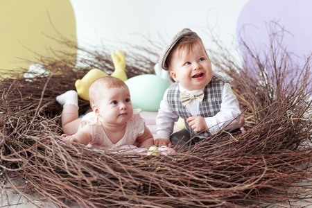 Little boy and girl sitting in natural nest with colorful Easter eggs. Home decoration - pastel color bunny banner. Looking to right sideの写真素材