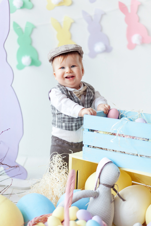 Funny happy baby boy in hat, tie bow and suit playing with Easter eggs. Rabbit banners on wallの写真素材