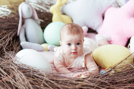 Cute little baby with colorful Easter eggs and toy rabbit lying in nestの写真素材