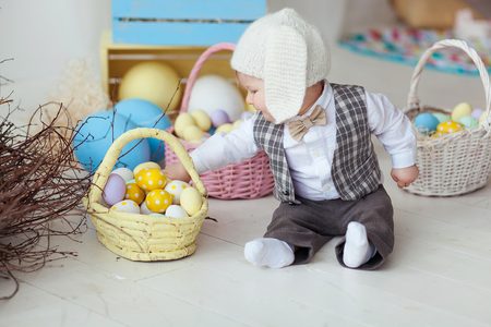 Funny happy baby boy in hat, tie bow and suit playing with Easter eggs. Rabbit banners on wallの写真素材