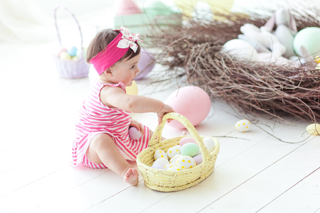 Cute little girl in red dress with Easter eggs sitting on floor at homeの写真素材