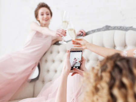 Attractive young bride and two bridesmaids making faces while taking selfie in the fitting room while drinking champagneの写真素材