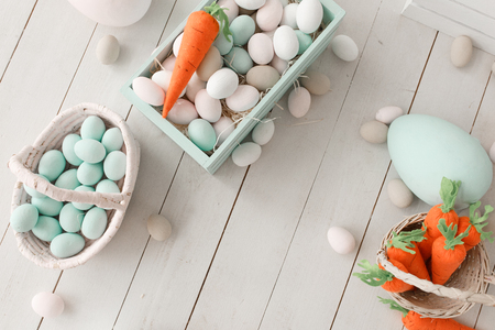 Easter background with colorful eggs and yellow orange carrots over white wood. Top view with copy spaceの写真素材