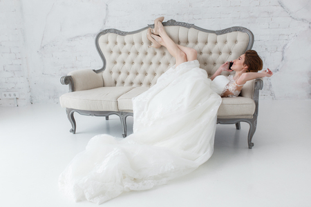 Tender bride talking over cell phone lying on classic sofaの写真素材