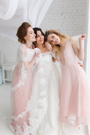 Happy bridesmaid hugging the bride in the bedroom in the morningの写真素材