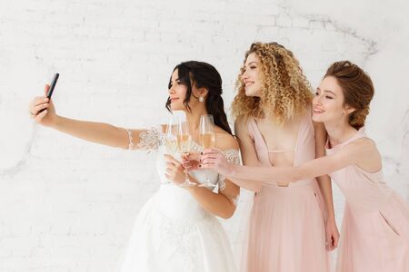 Smiling young girls taking a selfie together. Bride and bridesmaid making morning photoの写真素材