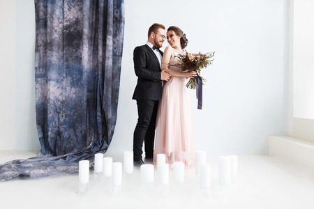 Full-length portrait of pretty newlyweds with bouquet. isolated white background and blue curtain. Studio horizontal shot with dry ice smokeの写真素材
