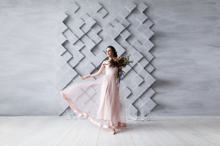 Beautiful bride in beige wedding dress with bridal bouquet dancing in studio isolated on gray background with copyspaceの写真素材