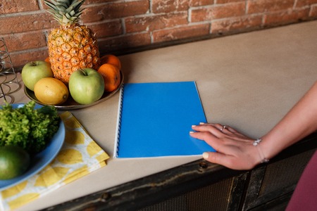 Healthy Food. Woman Hand on blue notebook, kitchen table with pineapple and fruitの写真素材