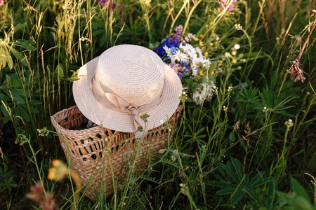 beautiful bouquet of lupines lies in a bag together with a straw hat on the grass in the field. Horizontal shotの写真素材