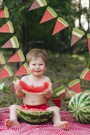 Baby blond boy eat watermelon and smile. Child has healthy eating habits. Looking forward to camera, funny lookの写真素材