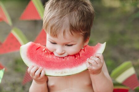 Baby blond boy eat watermelon and smile. Child has healthy eating habitsの写真素材