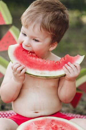 Baby blond boy eat watermelon and smile. Child has healthy eating habitsの写真素材