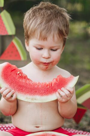 Baby blond boy eat watermelon and smile. Child has healthy eating habitsの写真素材