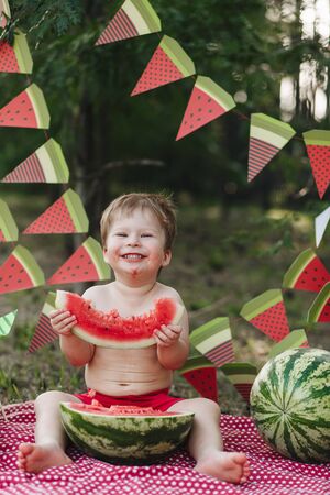 Happy baby blond boy eat watermelon and smile. Child has healthy eating habits. Looking forward to camera, funny lookの写真素材
