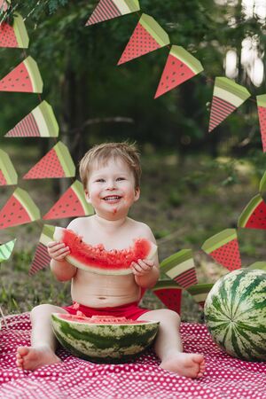 Happy baby blond boy eat watermelon and smile. Child has healthy eating habits. Looking forward to camera, funny lookの写真素材