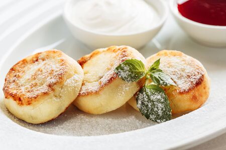 Cheesecake, fresh jam and mint. Cottage cheese pancakes or curd fritters decorated powdered sugar in plate close view. Healthy and diet breakfastの写真素材