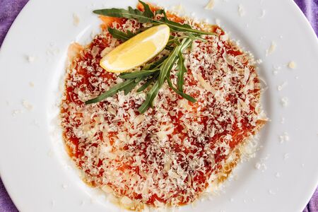 Carpaccio of salmon covered with parmesan, arugula and lemon slice. Top viewの写真素材