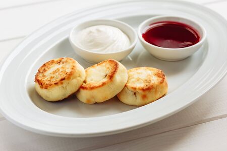 Summer cottage cheese pancakes on white plat on a wooden table with sour cream and jam, closeup, selective focusの写真素材