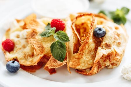 closeup of pancakes with strawberry and blueberry on plate on white background, decorated with mint leavesの写真素材
