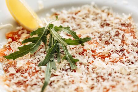 Carpaccio of salmon covered with parmesan, arugula and lemon slice. Close side viewの写真素材