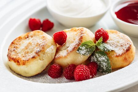 Close cheese pancakes, syrniki, curd fritters with fresh raspberries on white plate backgroundの写真素材