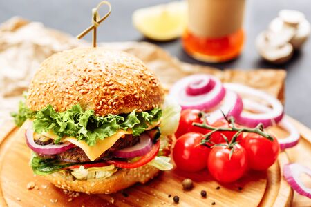 Close-up of home made tasty burgers on wooden table. Decorated with onion, cherry tomatoes and black pepperの写真素材