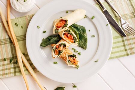 Rolls of thin pancakes with smoked salmon, horseradish cream cheese and spinach leaves. Side view with copy spaceの写真素材