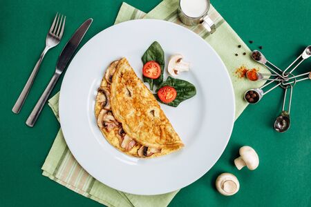 Omelet with mushrooms served on white plate with cherry tomatoes and spinachの写真素材