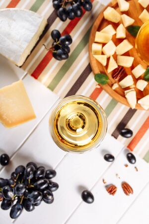 Glass of white wine, Cheese plate with mozarella, parmesan, honey and grapes on table. Top view selective focusの写真素材