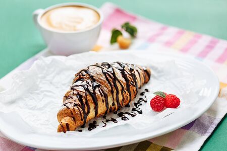Fresh homemade croissants and cappuccino on cloth napkin decorated with raspberry and chocolate topping. Side view with copy space on green backgroundの写真素材