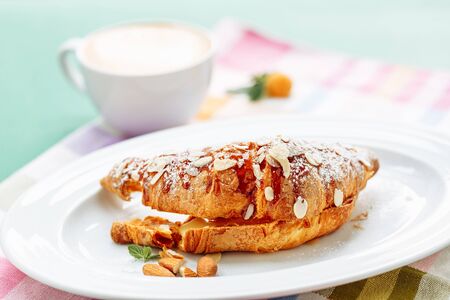 fresh croissants covered with jam and sliced almond on blurred coffe cup background for breakfastの写真素材