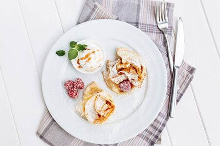 Crepes Pancakes with fruit jam and ice cream. Top view on white wooden table decorated with sugar powderの写真素材