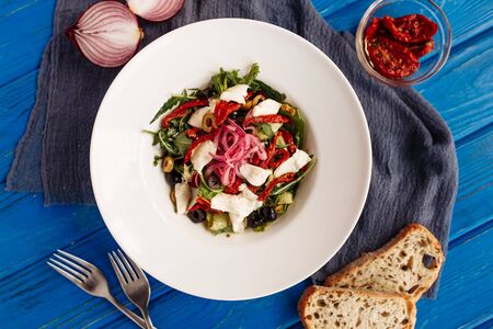 Fresh salad with sun-dried tomatoes, olives, arugula and onion. Close side view decorated on tableの写真素材