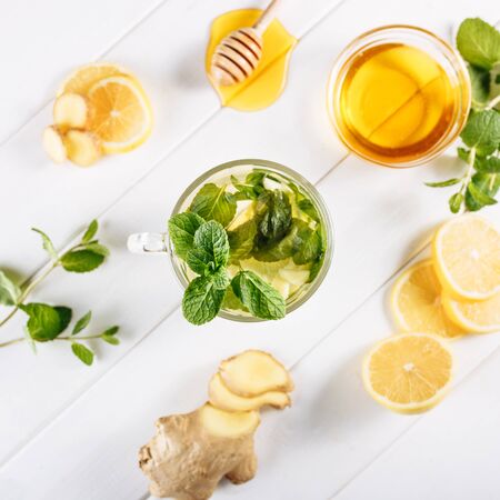 Ginger green tea in a glass for flu cold winter days. Side view on white wooden background decorated with mint, lemon and honeyの写真素材