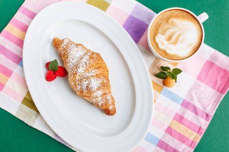 Fresh homemade croissants and coffee on cloth napkin decorated with raspberry. Top view with copy space on green backgroundの写真素材