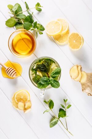 Ginger green tea in a glass for flu cold winter days. Side view on white wooden background decorated with mint, lemon and honeyの写真素材