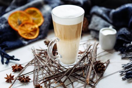 Glass cup of coffee latte on wooden table decorated with plaid, wood sticks and dried orange slicesの写真素材