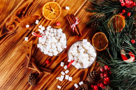 Homemade two Cocoa glasses with Marshmallows. Hot winter drink on wooden Backdrop decorated with cinamon sticks and fir branches. Top view copy spaceの写真素材